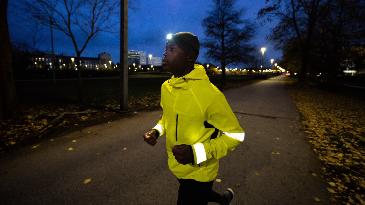Runner in reflective gear and a headlamp on a lit path at dusk, training after daylight saving time ends
